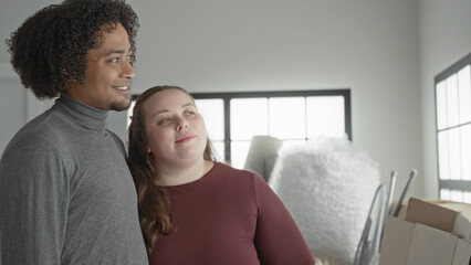 Fototapeta premium Man and plus size woman lean together with head on shoulder, holding moving boxes inside building; affection moving together.