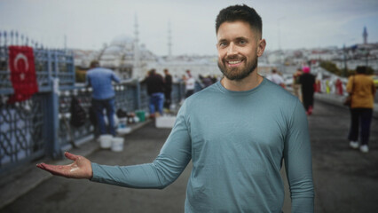 Fototapeta premium Hispanic man with beard smiling and extending hand toward the camera on a busy street near fishermen and a turkish flag; friendly greeting.