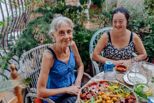Smiling senior woman and adult woman with Down syndrome enjoying outdoor family meal together
