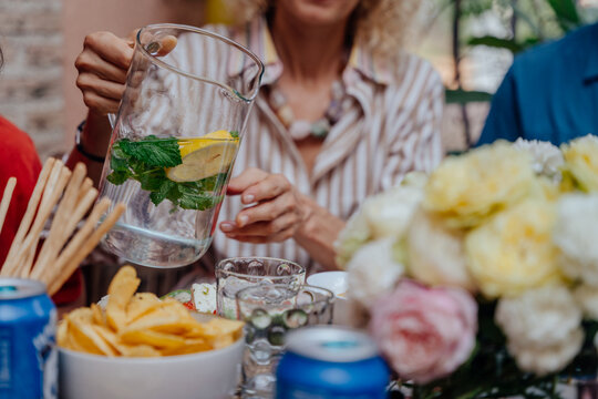 Adult woman serving lemon mint infused water during relaxed outdoor Mediterranean lunch gathering