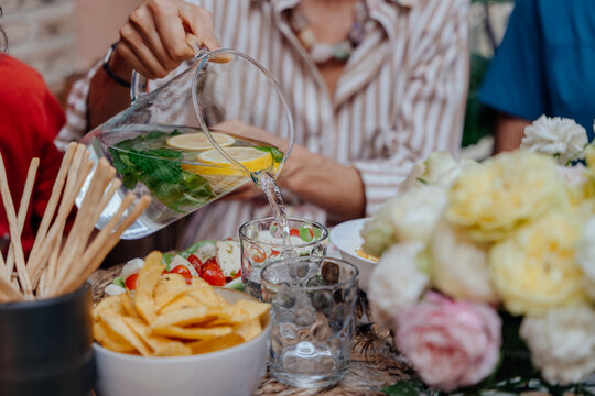 Adult woman pouring lemon mint water into glass during relaxed Mediterranean outdoor lunch