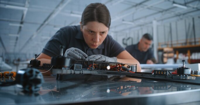 Professional Female Specialist Builds FPV Drone Frame on Industrial Assembly Line, Representing Modern Defense Manufacturing Advanced Aerospace Production in Large Factory. Concept of Production Line.