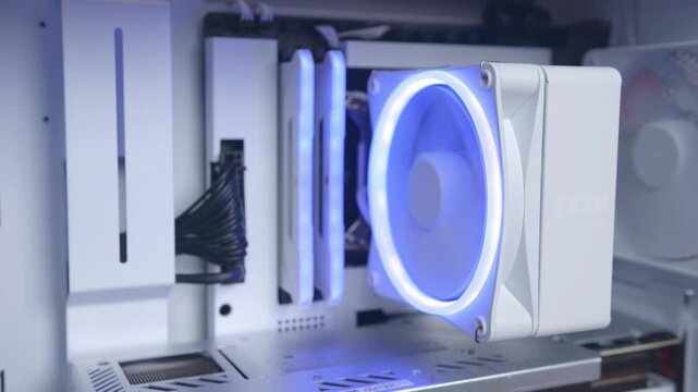 Close-up of white desktop computer interior with glowing blue ring LED cooling fan and illuminated RAM memory modules inside open case, cables and vents visible