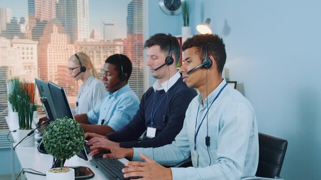 A diverse group of call center agents wearing headsets and professional attire working collaboratively at their desks in a bright office with cityscape views.