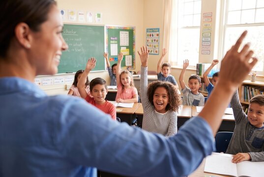 Diverse group of elementary school children raising hands in a classroom during a lesson with a female teacher, capturing active student participation for primary education marketing.