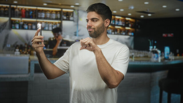 Man holding smartphone with finger pointing to screen at bar counter inside a building; curiosity connection.