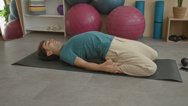Man on mat kneeling in a supported backbend with hands holding heels in a studio; serenity mindfulness.
