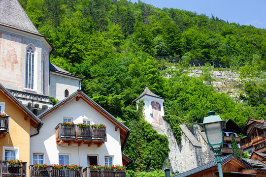 Historic Church and Houses with Flowers on Balconies in Hallstatt Austria against Green Mountains.