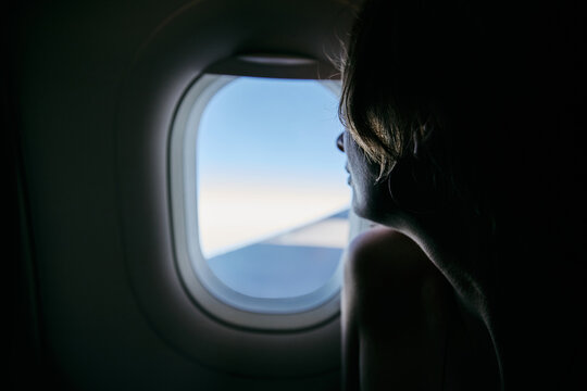 Silhouette of woman looking through airplane window during flight