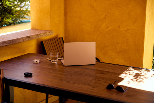 Remote Work Setup with Laptop and Sunglasses on Sunny Outdoor Terrace Table