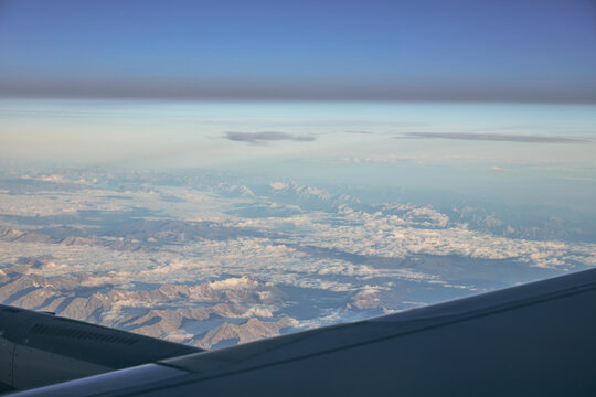 Aerial view of snowy mountain ranges and clouds seen from airplane window