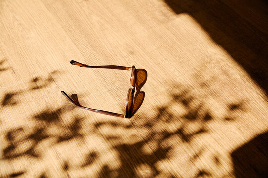 Stylish Sunglasses on Wooden Surface with Sunlight and Plant Shadows