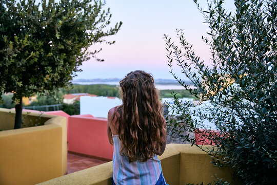 Rear View of Woman with Long Wavy Hair Looking at View from Balcony
