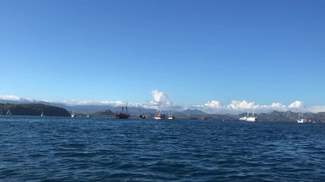 Scenic view of sailboats anchored in a calm blue bay under a clear sky in NTT, Flores, Indonesia.