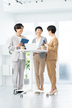 明るいオフィスで立ち会議をする笑顔のビジネスパーソン3人