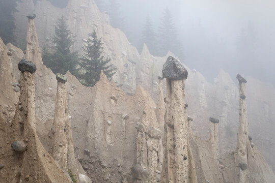 Misty Earth Pyramids with Large Capstones in a Mountain Forest, Atmospheric Foggy Landscape and Natural Rock Formations