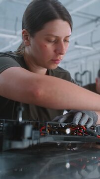 Skilled Female Technician Manually Assembles FPV Drone Frame on Modern Industrial Production Line. Woman Demonstrating Precision Aerospace Manufacturing in Modern Defense Technology Facility. Vertical