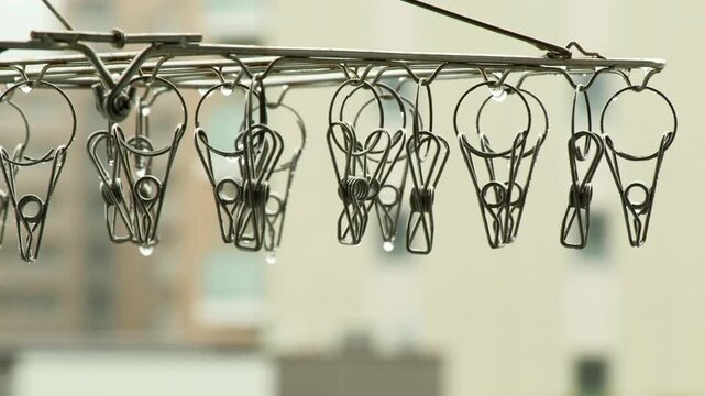 雨の日のベランダに佇むステンレス洗濯ピンチと滴る水滴のマクロ映像