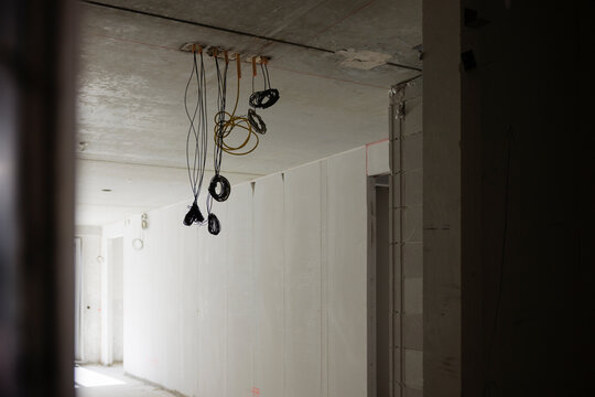 Interior of an unfinished building under construction showing bare concrete walls and ceiling with electrical wiring and conduits hanging down in preparation for outlet installation