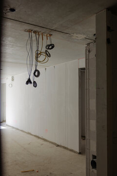 Interior of an unfinished building under construction showing bare concrete walls and ceiling with electrical wiring and conduits hanging down in preparation for outlet installation