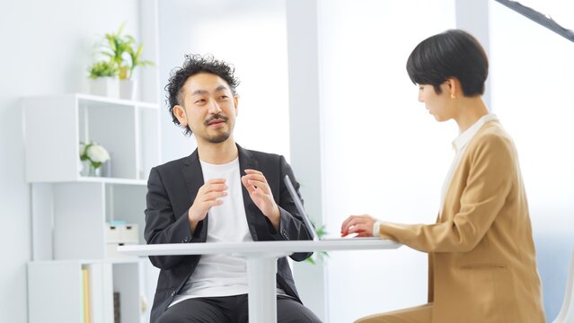 明るいオフィスで手振りを交えて話す男性と記録する女性