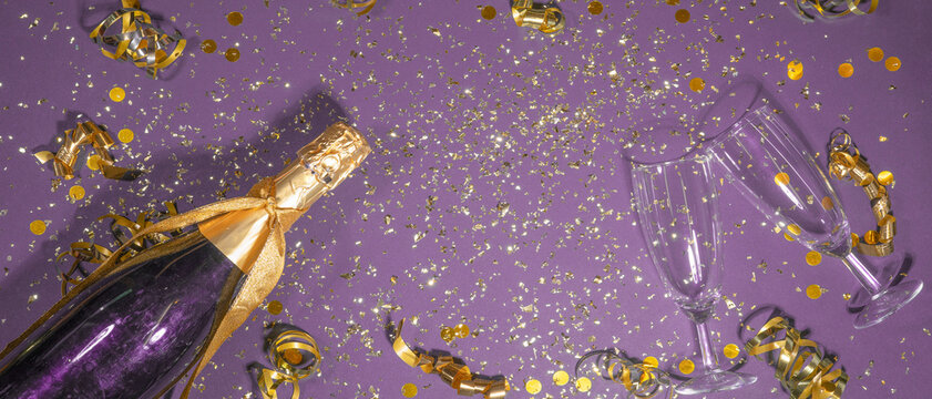 Happy New Year 2027, New Year's Eve Party Celebration Greeting Card - Golden Champagne Bottle, Champagne Or Sparkling Wine Glasses and Ribbons Frame, Isolated On Purple Table Background, Flat Lay