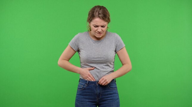 Frustrated woman struggling to button tight jeans on green screen