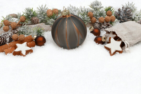 Festive background featuring a modern Christmas bauble, cinnamon sticks, and cinnamon star cookies in the snow, with plenty of copy space.