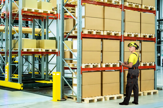 Warehouse. Inventory specialist checks palletized cargo with a tablet while monitoring warehouse storage, stock control and distribution center operations.
