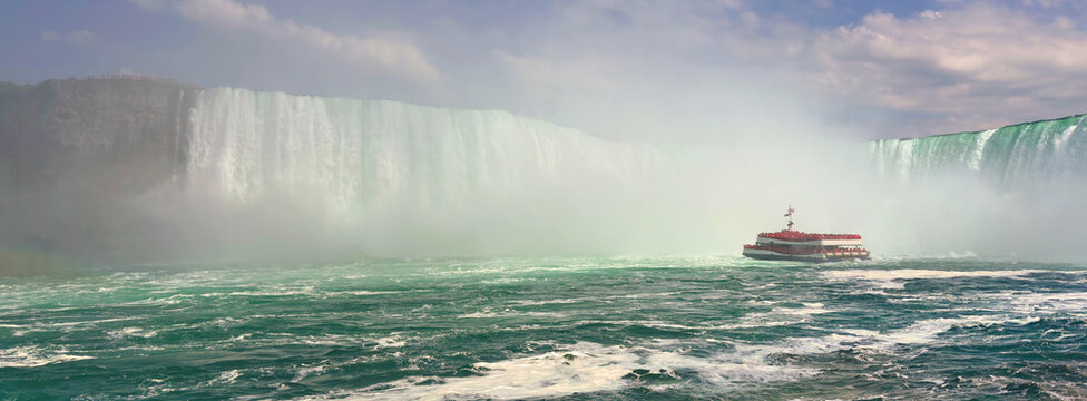 A panoramic of Niagara Falls with a tour boat and mist. A breathtaking panoramic view of Niagara Falls captures the immense power and beauty of nature. 