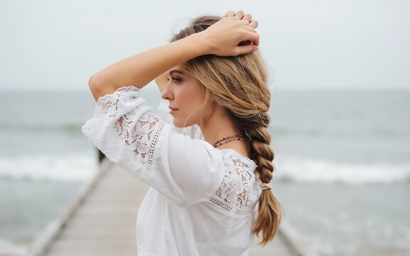 Young woman with braided hair standing on a wooden pier by the ocean