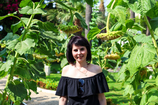 Portrait of an adult woman in off shoulder clothing,  sun-drenched alley among blooming yellow sunflowers and tall palm trees.