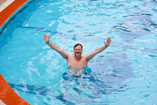 Happy adult man swimming and relaxing his own small private backyard swimming pool near a house on a sunny warm summer day.