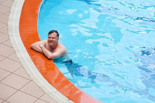 Happy adult man swimming and relaxing in his own small private backyard swimming pool near a house on a sunny warm summer day.