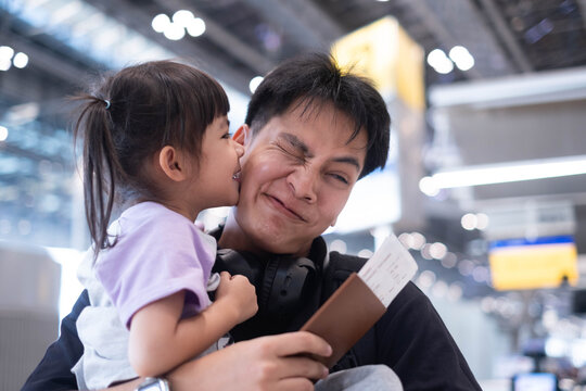 Father sharing a playful kiss with his daughter at an airport while holding a passport and boarding pass, capturing family love, travel, vacation, international adventure, a joyful journey together.