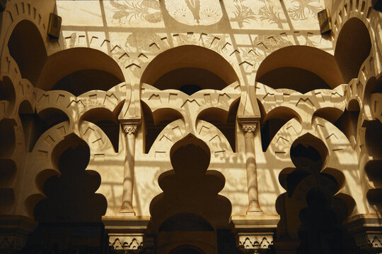 Intricate Moorish arches with dramatic sunlight and shadows in a Moroccan riad