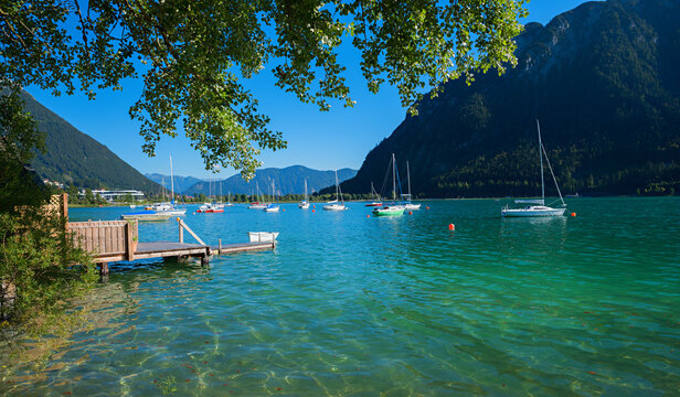 Idyllic Buchau Bay on Lake Achensee, with many sailboats and poplar branches.