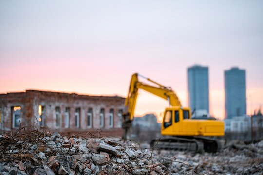 Yellow excavator standing at urban demolition site with rubble and city skyline urban redevelopment