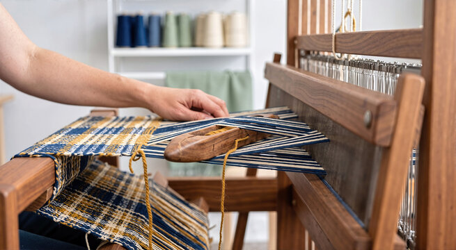 Hand weaving a colorful yarn pattern on a walnut wooden loom. Shuttle with mustard thread and indigo warp