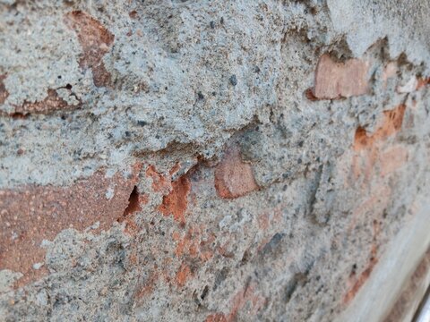 Cracked concrete wall layer revealing old red brick structure underneath close up view 