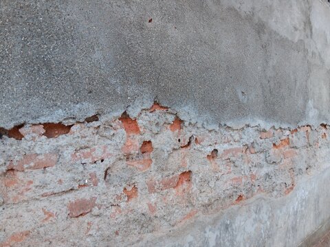 Cracked concrete wall layer revealing old red brick structure underneath close up view 
