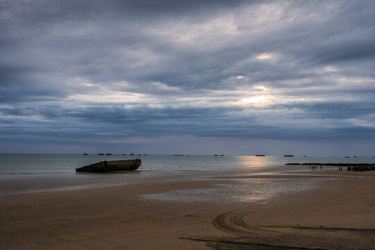 Rusty remains of a Mulberry harbour caisson on Gold Beach at Arromanches-les-Bains in Normandy under stormy sky.