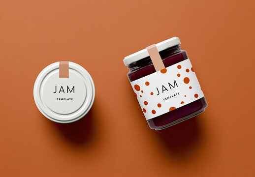 Two glass jars of jam, one upright, one on its side, on an orange surface