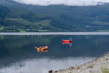 Two small motorboats on calm Norwegian fjord water with forested mountains © heerim studio