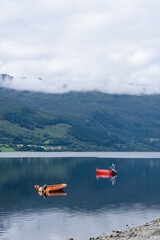 Two small boats floating on a calm Norwegian lake with forested mountains under a cloudy sky © heerim studio
