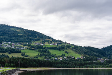 Fototapeta premium Norwegian village houses on a green hillside overlooking a calm lake under cloudy sky