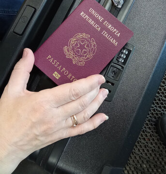 Hand Holding Italian Passport Over Suitcase for Travel Preparation.

