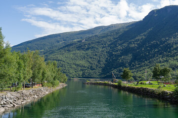 Obraz premium Scenic river view with green trees, rocky banks, and majestic mountains