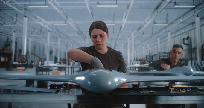 Young Woman Assembling Drone on Modern Production Line Inside Large High Tech Factory, Demonstrating Skilled Engineering, Precision Craftsmanship, Aerospace Technology and Industrial Innovation.