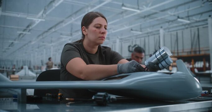 Focused Engineer Wearing Safety Gloves Meticulously Connects Battery Sensor Unit Wires to Main Drone Circuit. Bright Production Hall Emphasizes Precision Industrial Aviation Electronics Assembly.